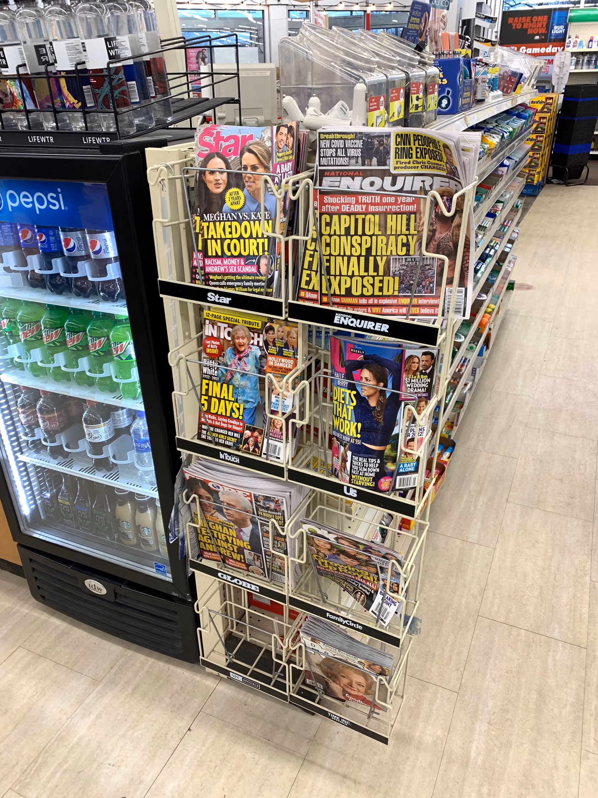 Magazine rack with tabloids beside a Pepsi fridge inside Discount Drug Mart.