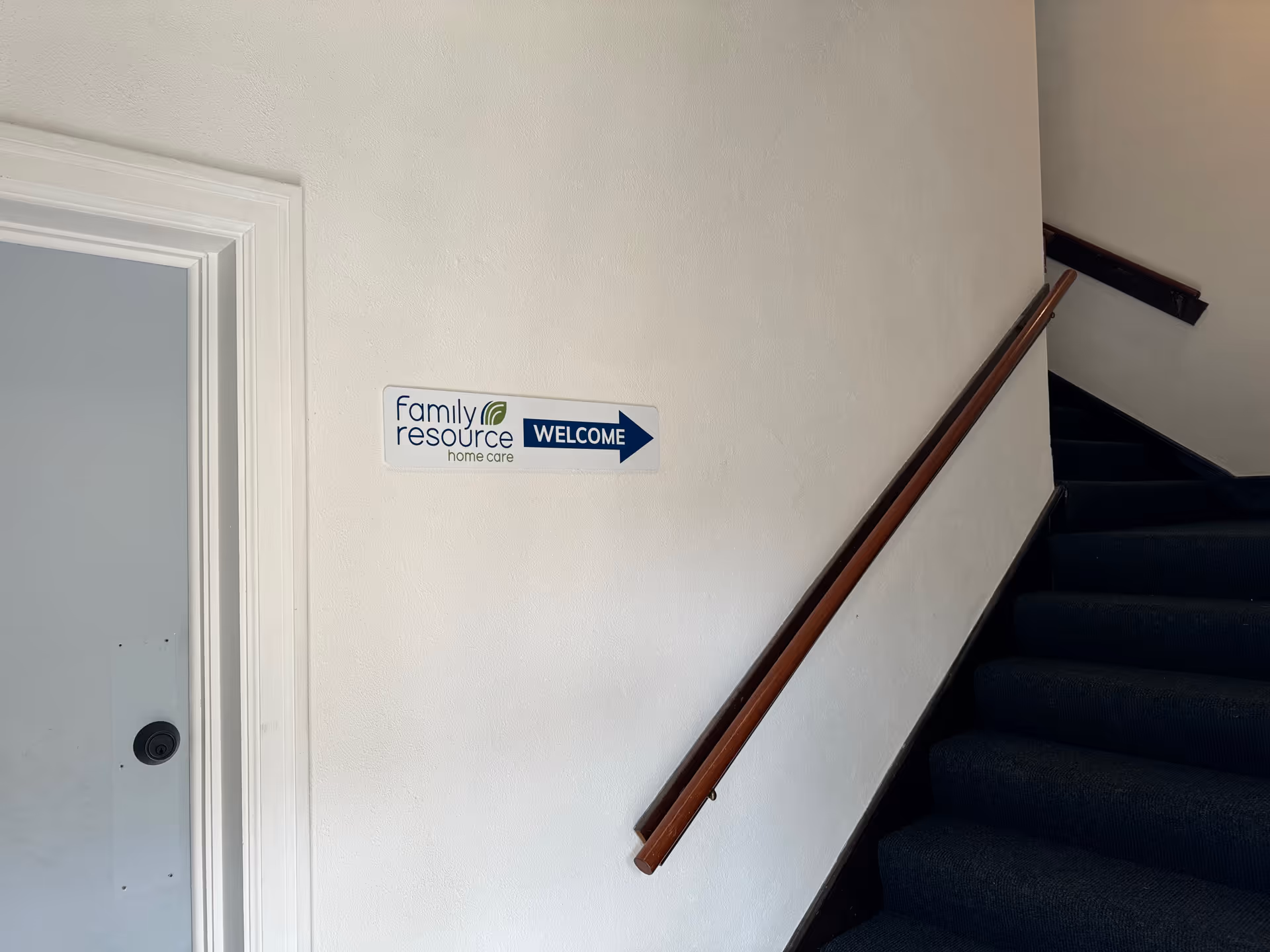 White interior stairwell with a wooden handrail and a Family Resource Home Care sign.