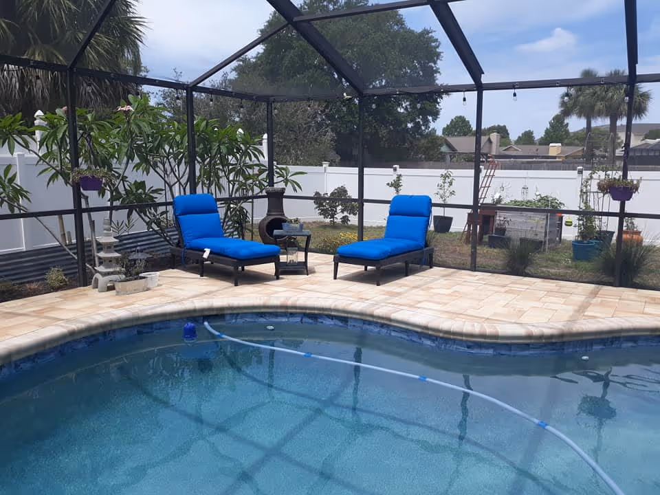 Enclosed outdoor pool area with blue lounge chairs and potted plants.