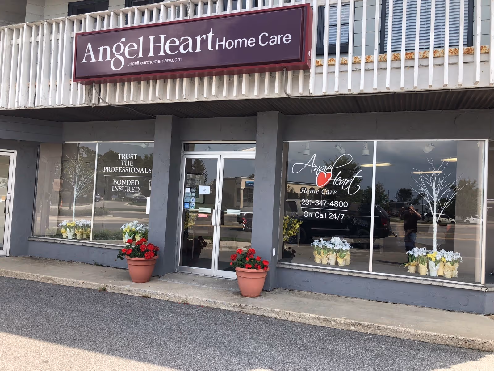 Front exterior of Angel Heart Home Care storefront with sign, glass windows, and potted flowers.