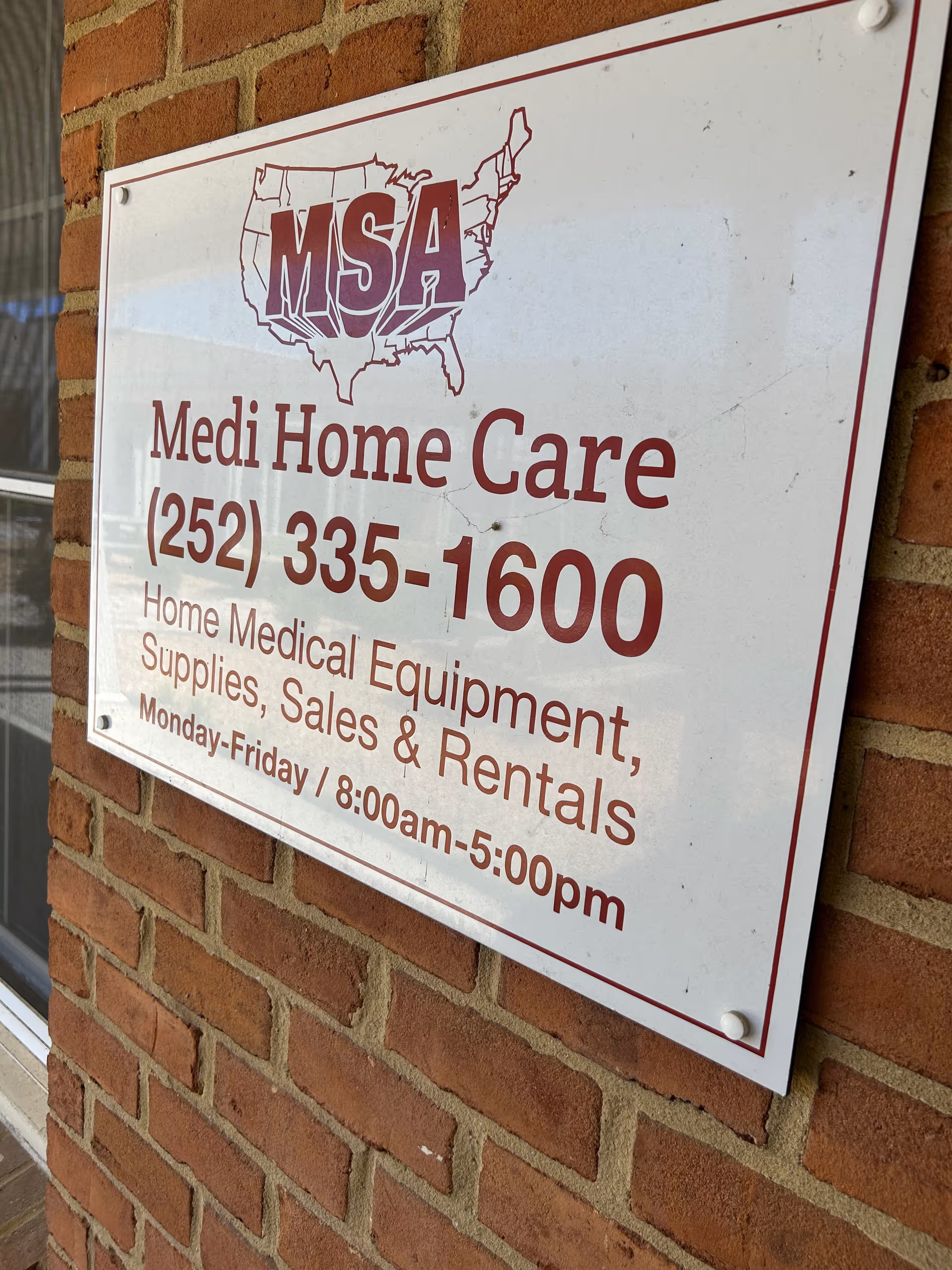 A Medi Home Care sign with a phone number mounted on a brick exterior wall.