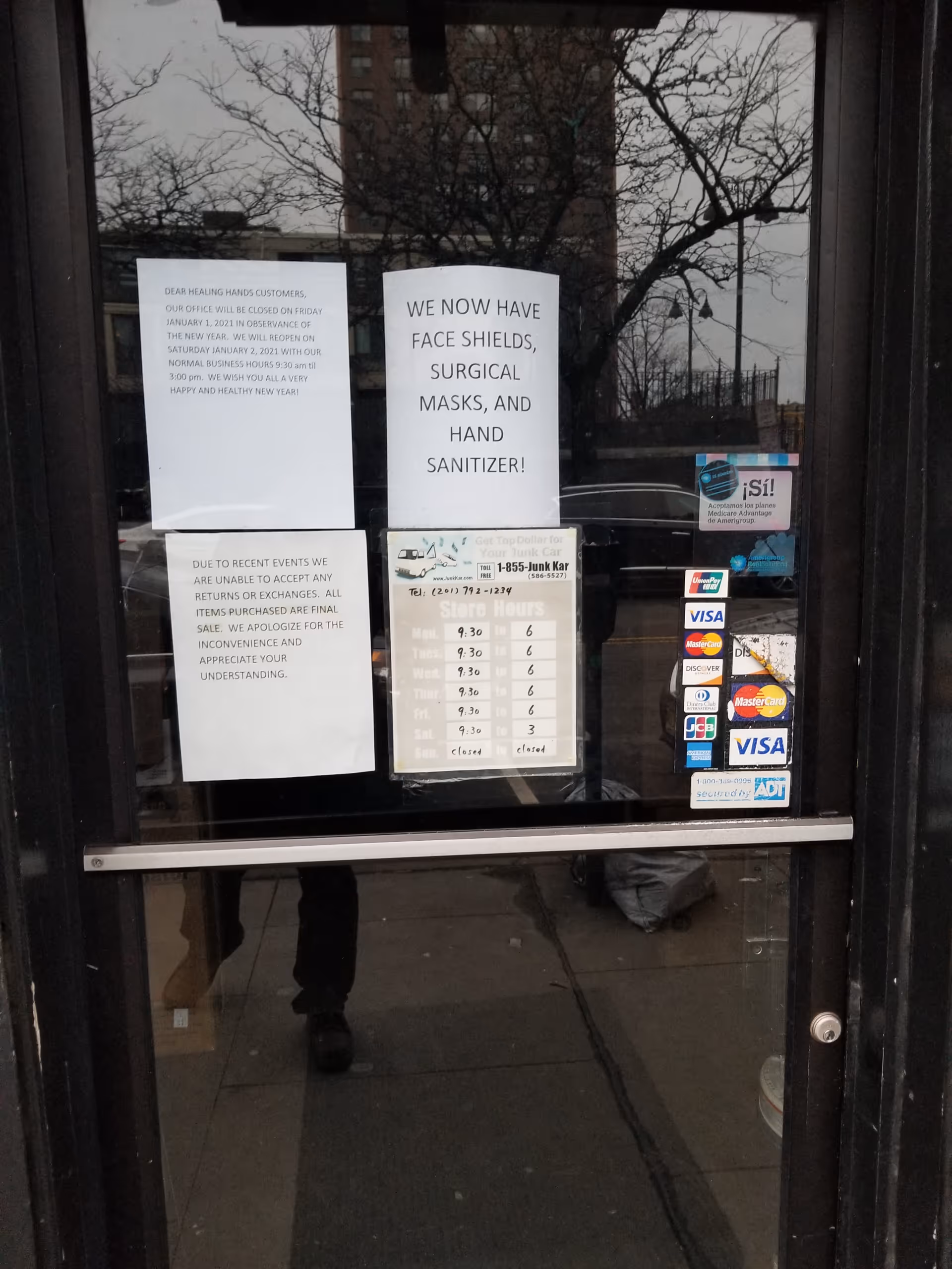 Glass door with posted notices and reflections of trees outside.