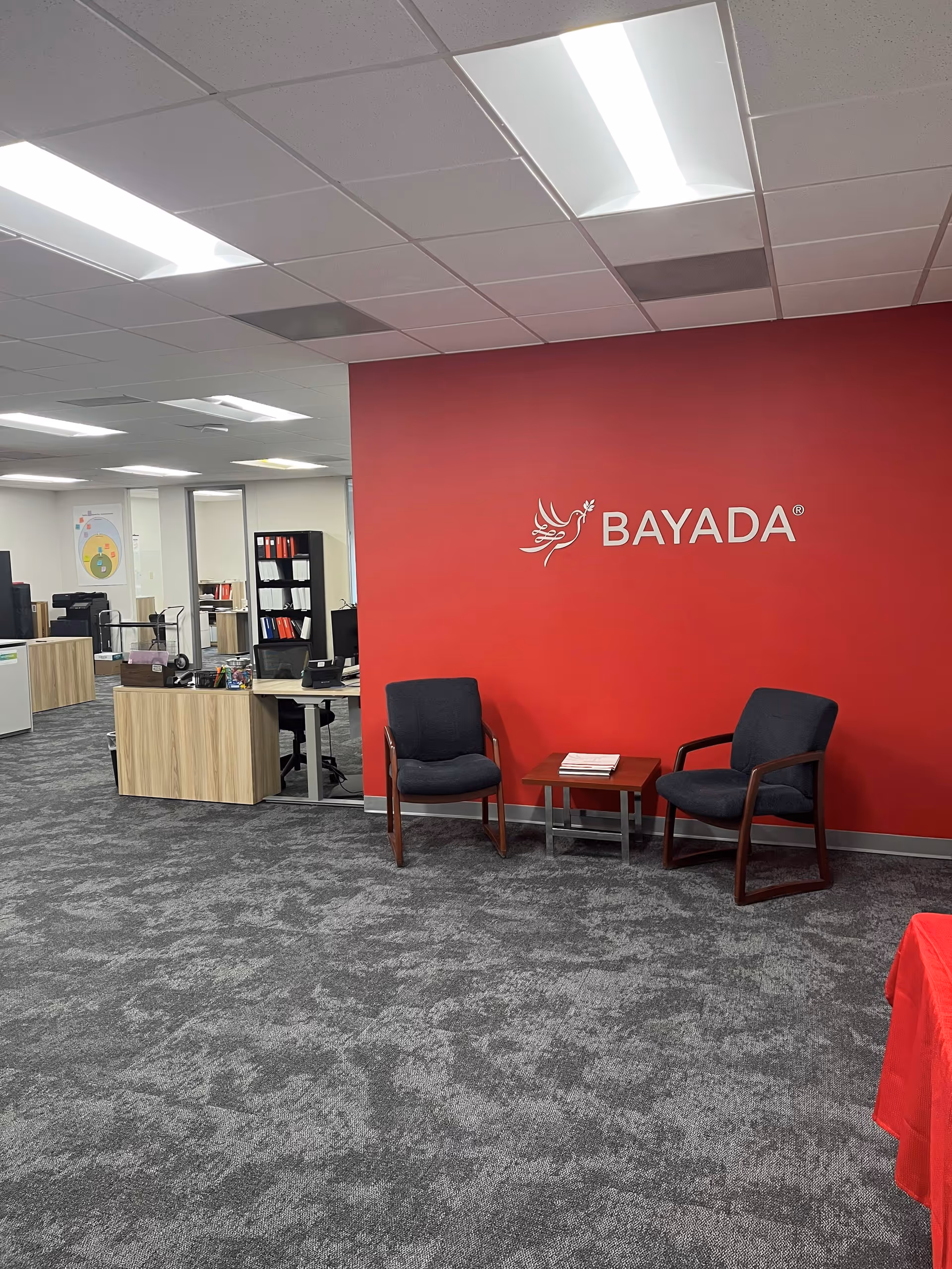 Office reception area with red BAYADA wall and two chairs near a small table.