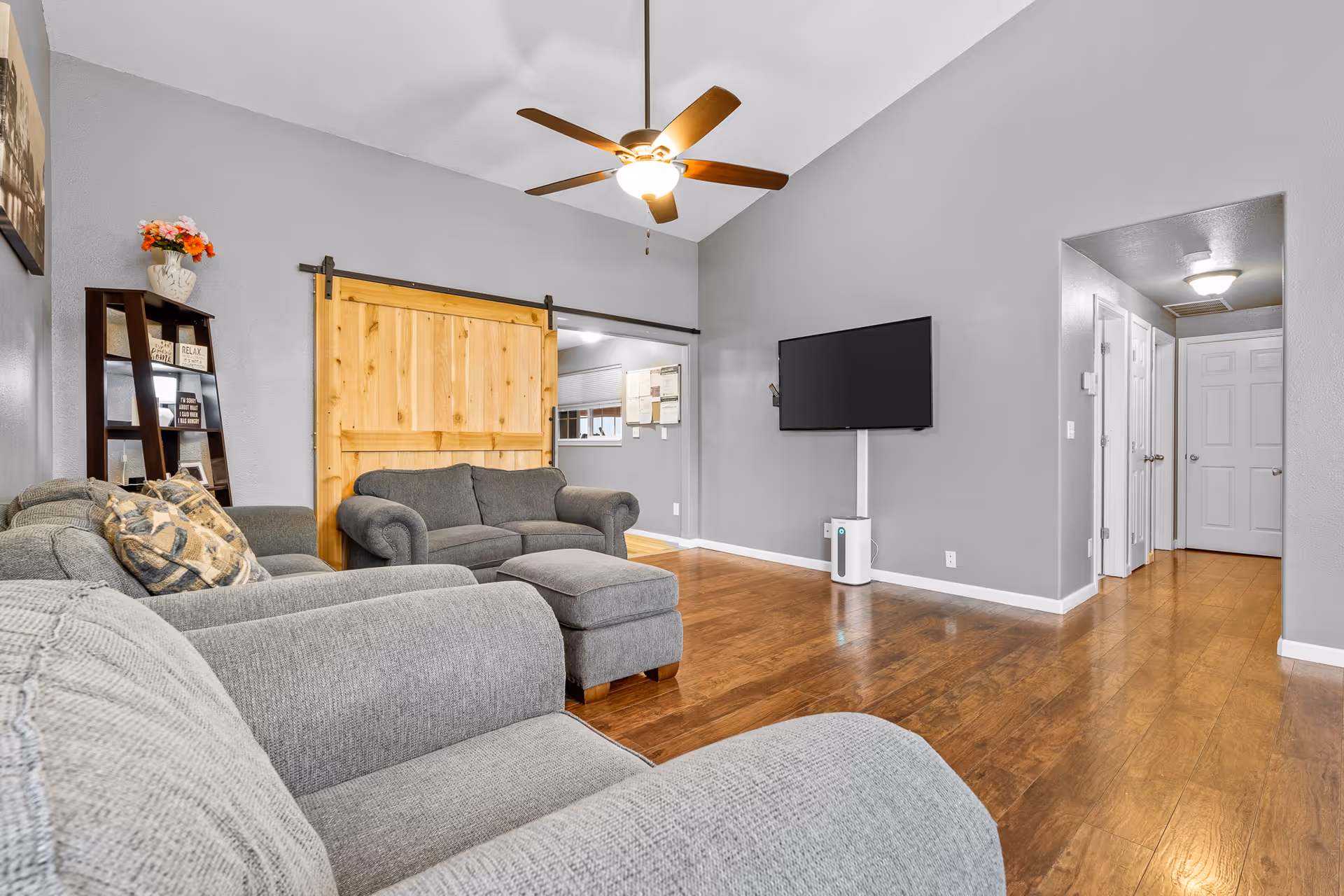 Gray sofas fill a cozy living room with a wall-mounted TV and wooden floors.