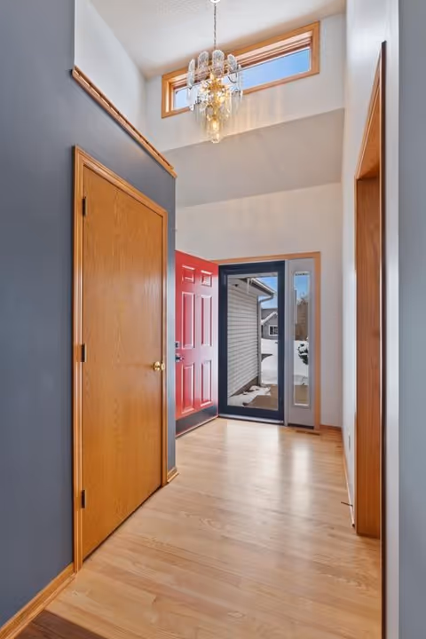 Interior hallway at the entrance with wooden doors, chandelier, and glass front door.