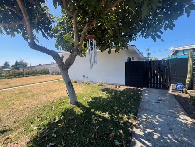 Exterior view of a white residential building with yard, tree, wind chimes, and gate.
