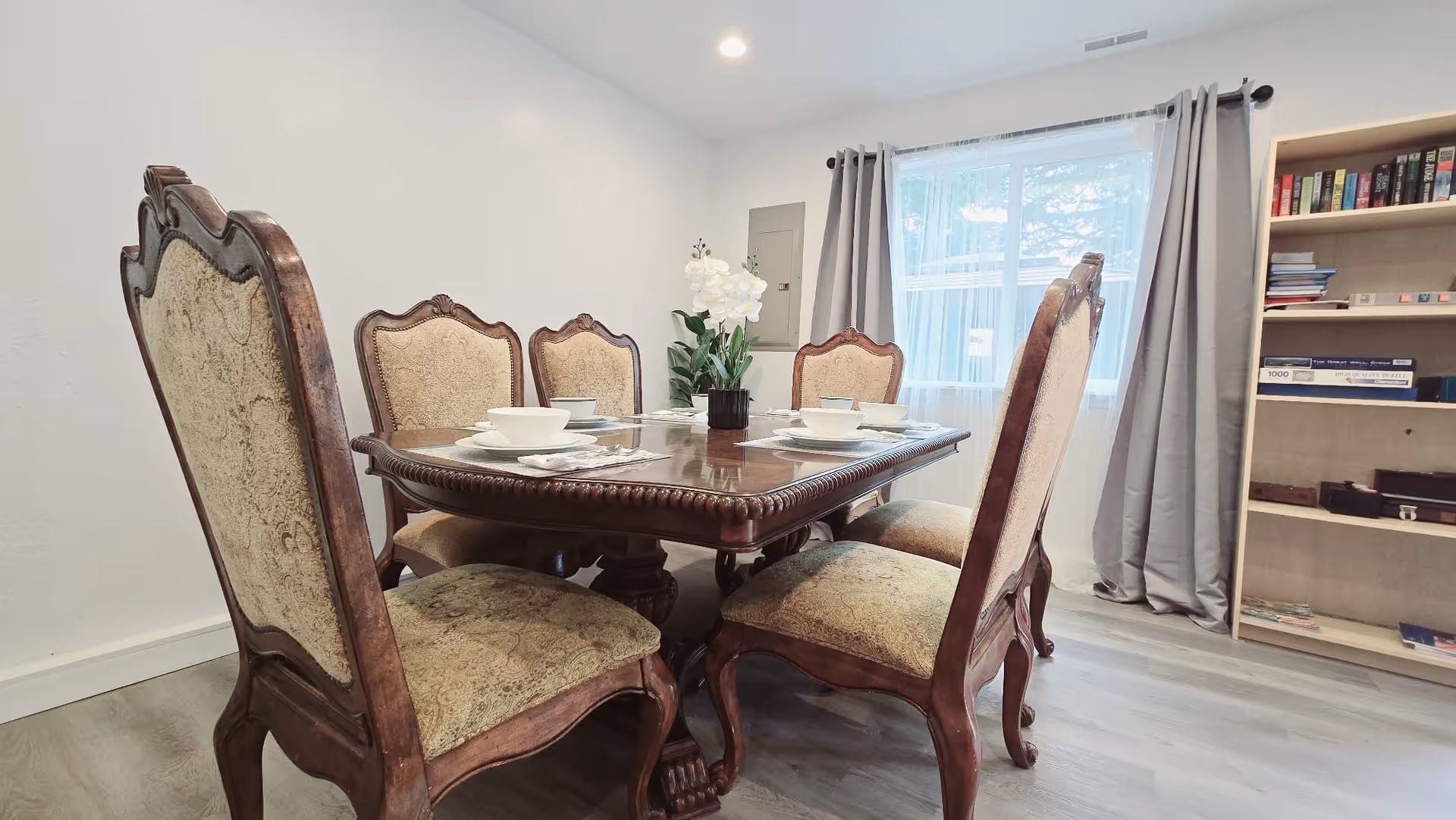 Traditional wooden dining table with ornate upholstered chairs in a bright, tidy dining room.