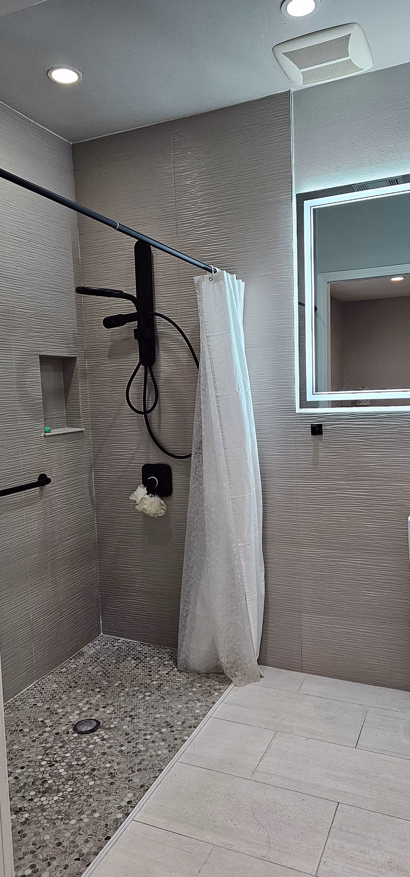 Shower area with curtain, handheld showerhead, grab bar, and pebble floor.