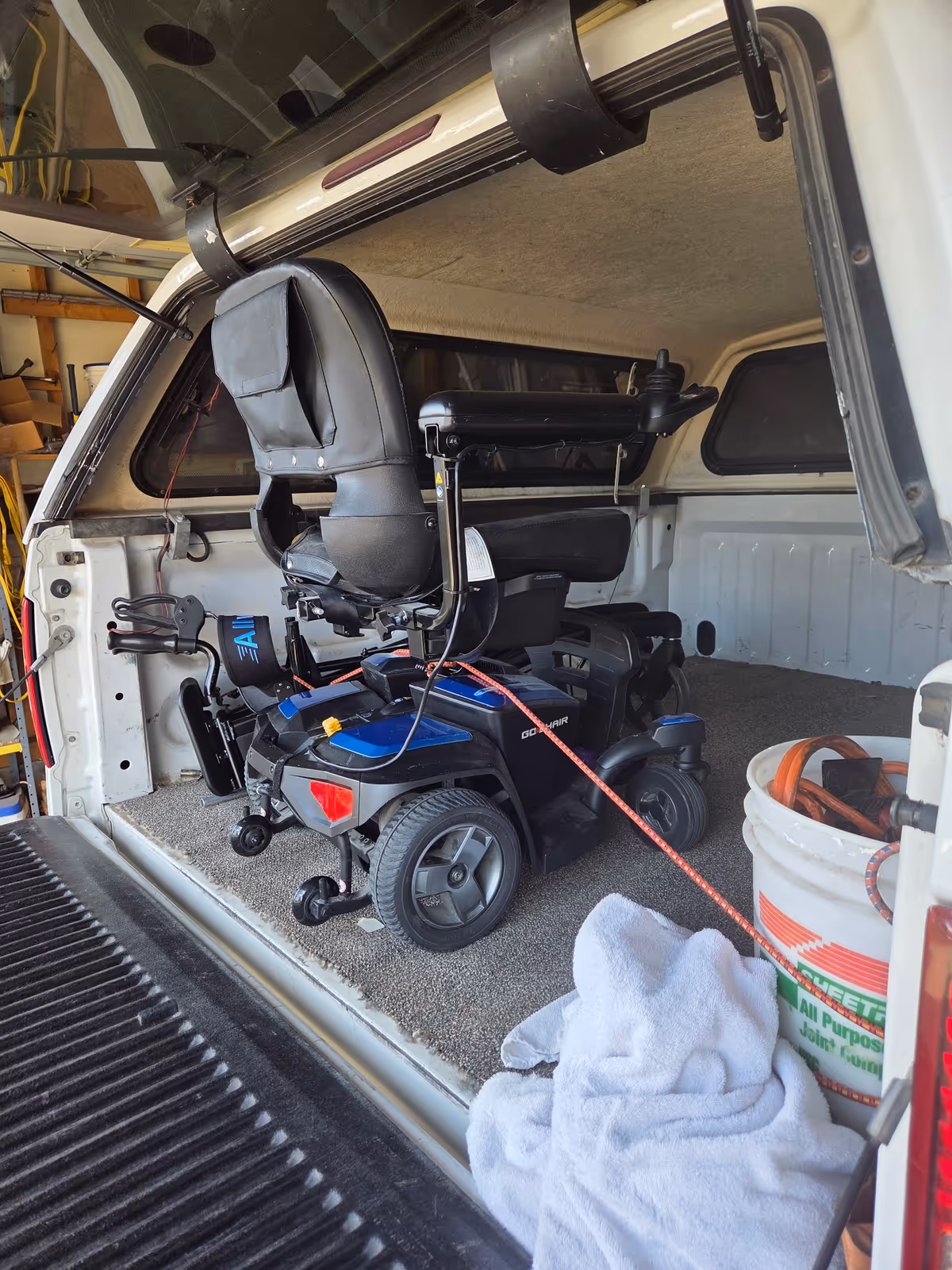 Inside a van cargo area, a powered wheelchair secured with straps.