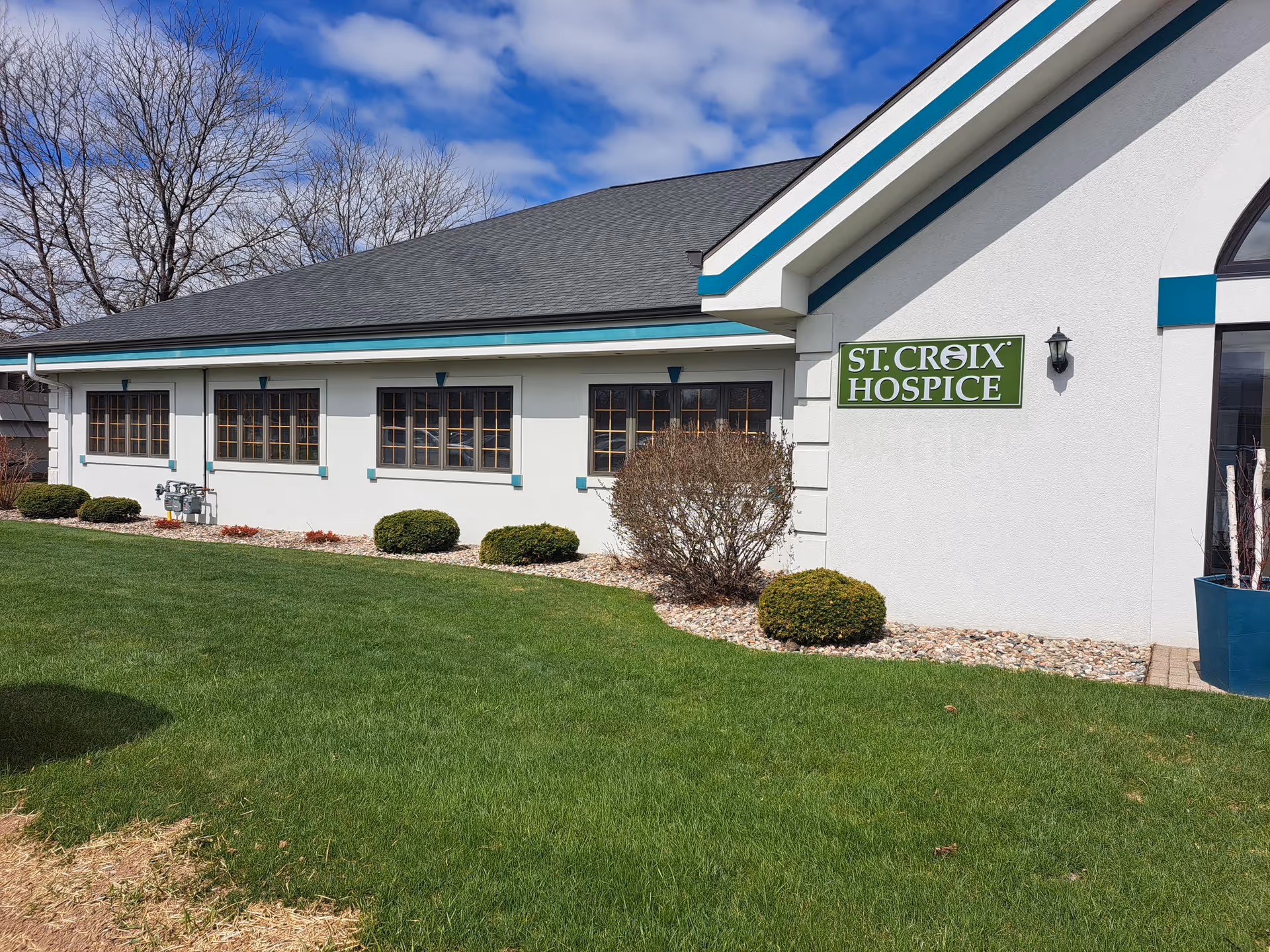 White hospice building with teal trim, St. Croix Hospice sign, and a manicured lawn.