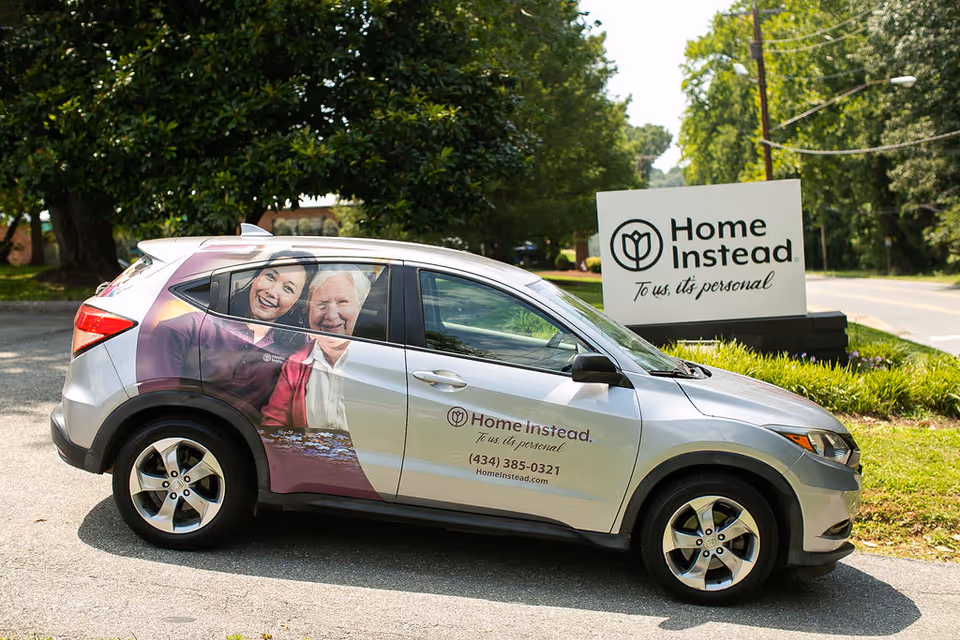 Silver Home Instead van parked outdoors beside a branded sign in a sunny lot.