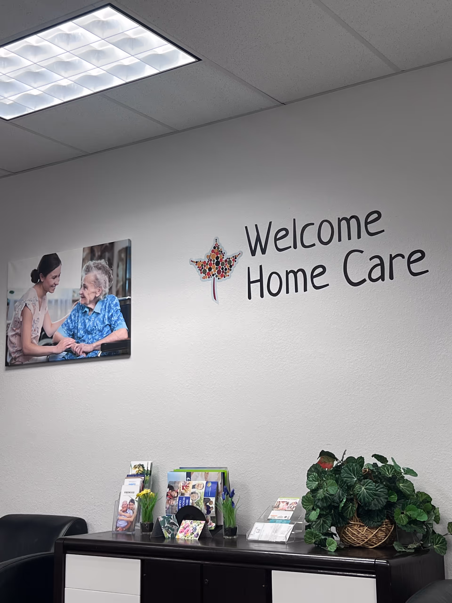 A reception area with a Welcome Home Care sign, brochure table, and plants.
