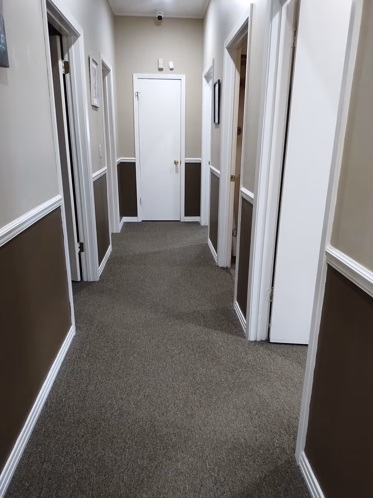 Interior hallway in a senior living facility with beige walls, white trim, and closed doors.