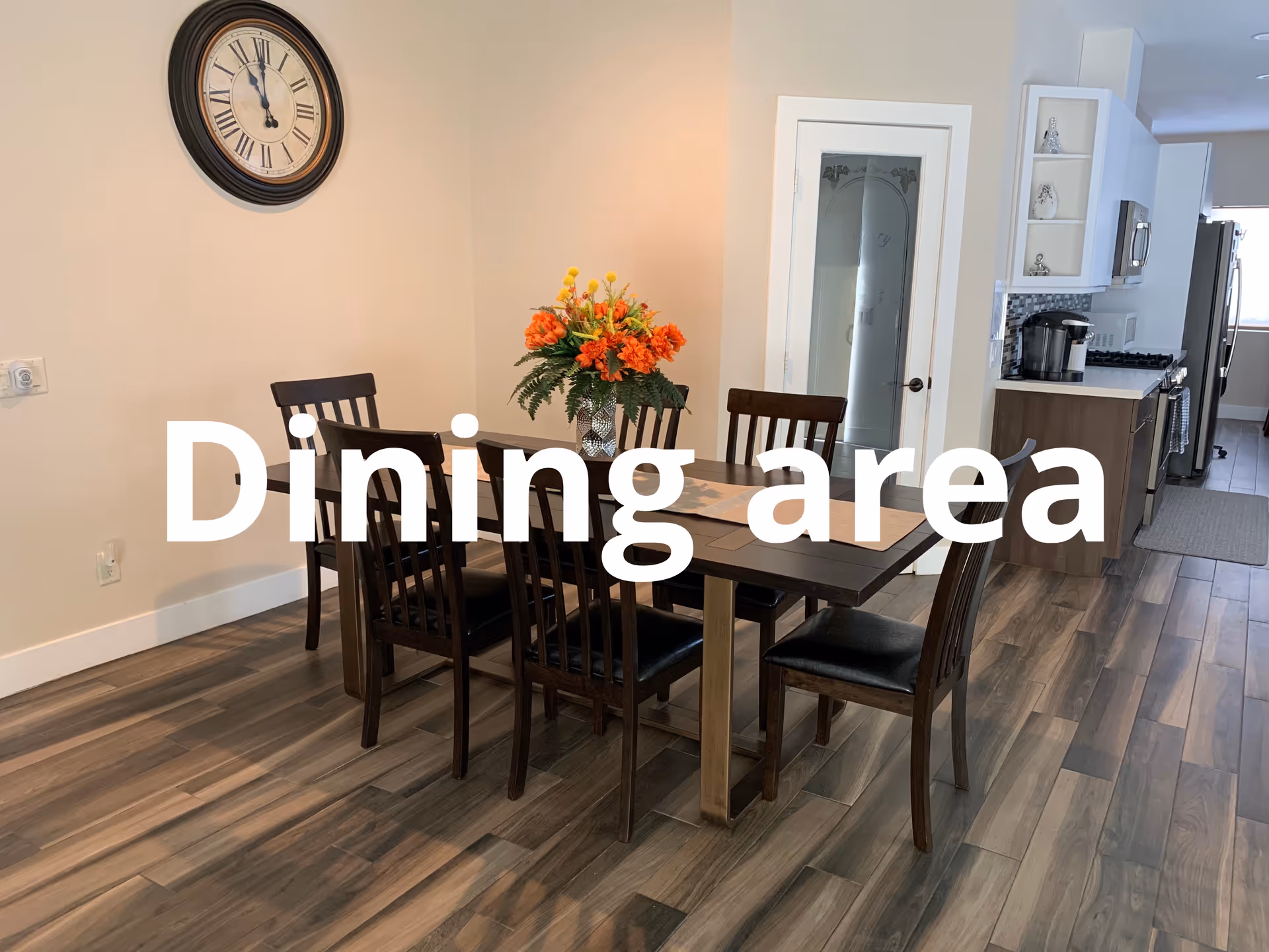 Dining room in a senior living facility with a table, chairs, centerpiece, and a nearby kitchen.