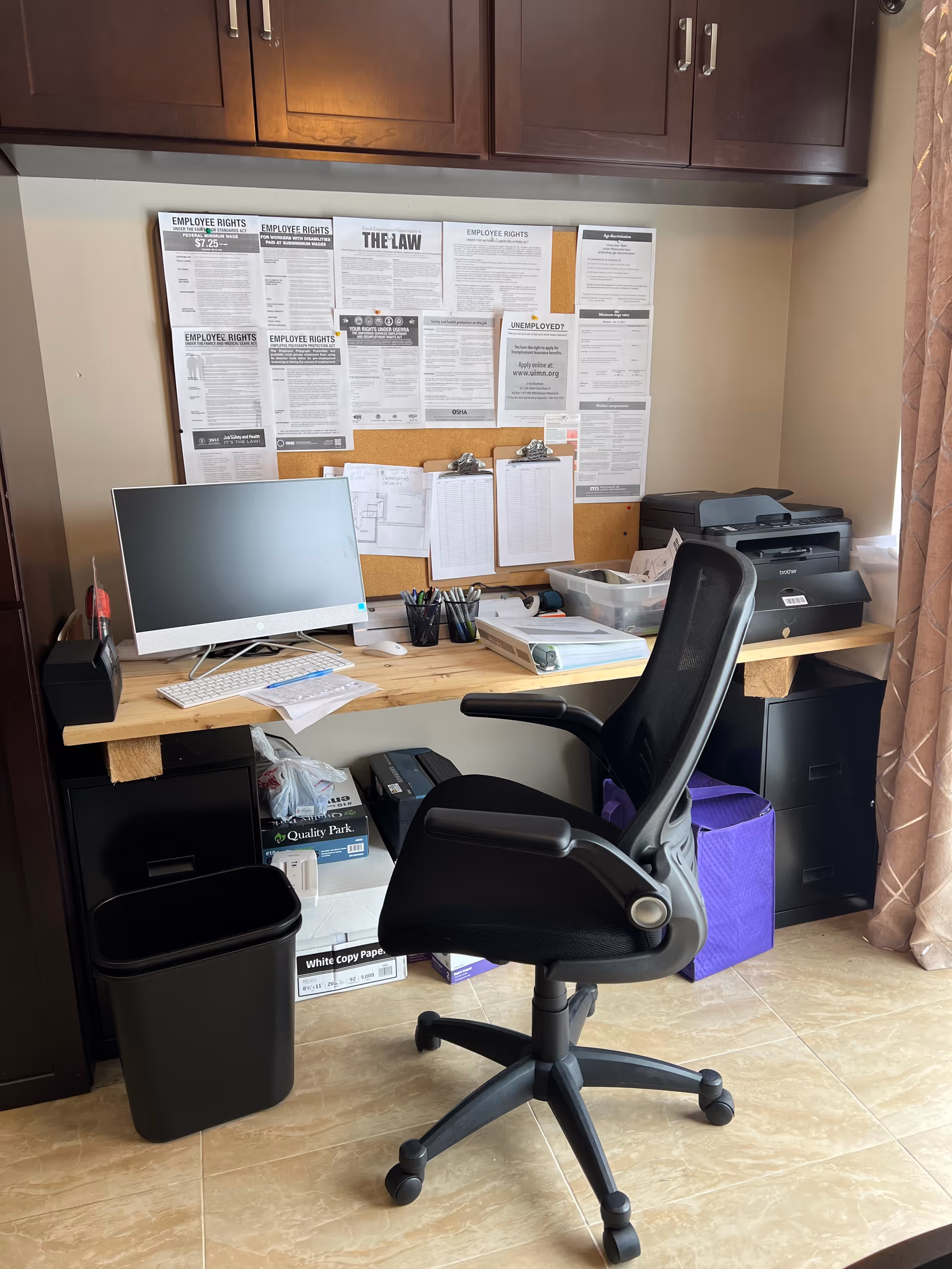 Office workstation in a senior living facility with computer, printer, corkboard, and filing supplies.