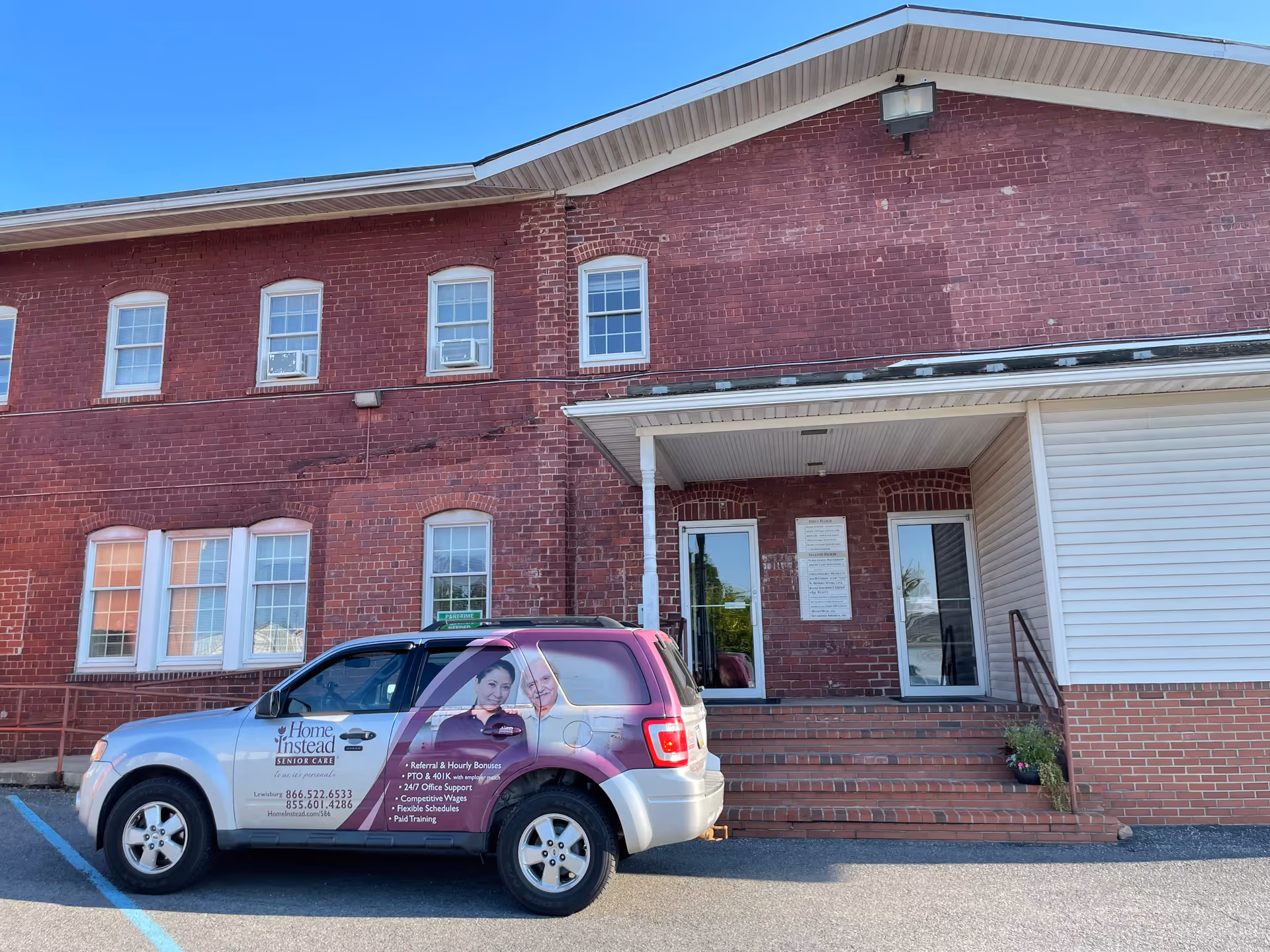 Brick senior care facility entrance with a parked Home Instead vehicle in front.