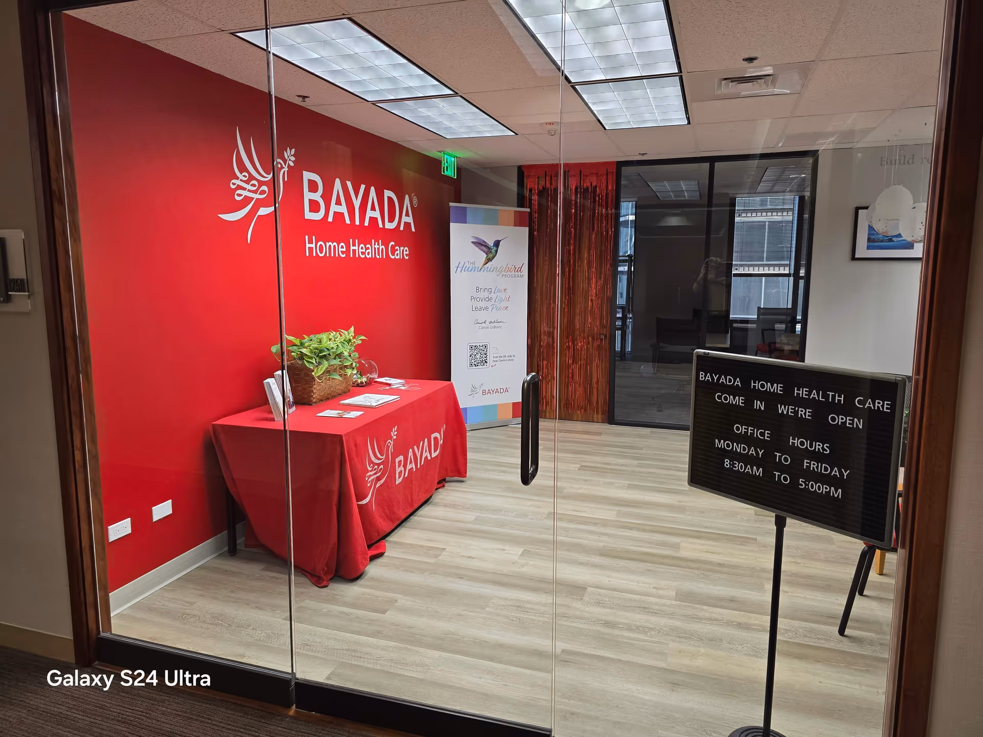 Interior BAYADA Home Health Care reception area with red branding, glass doors, and a sign.