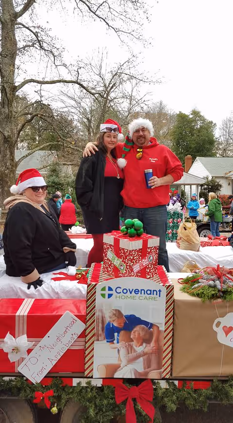 Smiling people in Santa hats atop a Christmas float with Covenant Home Care signage.