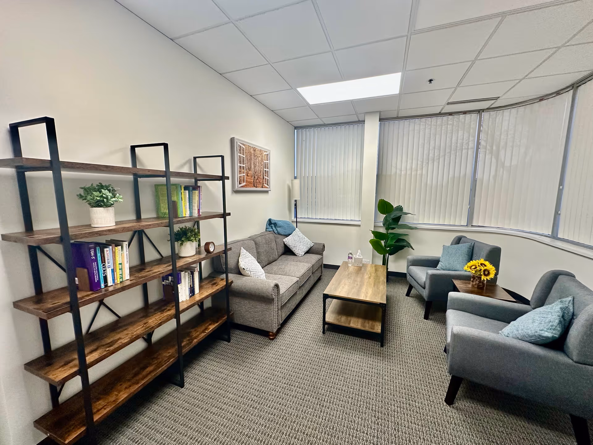 Cozy lounge area with gray sofas, a coffee table, bookshelves, plants, and curved windows.