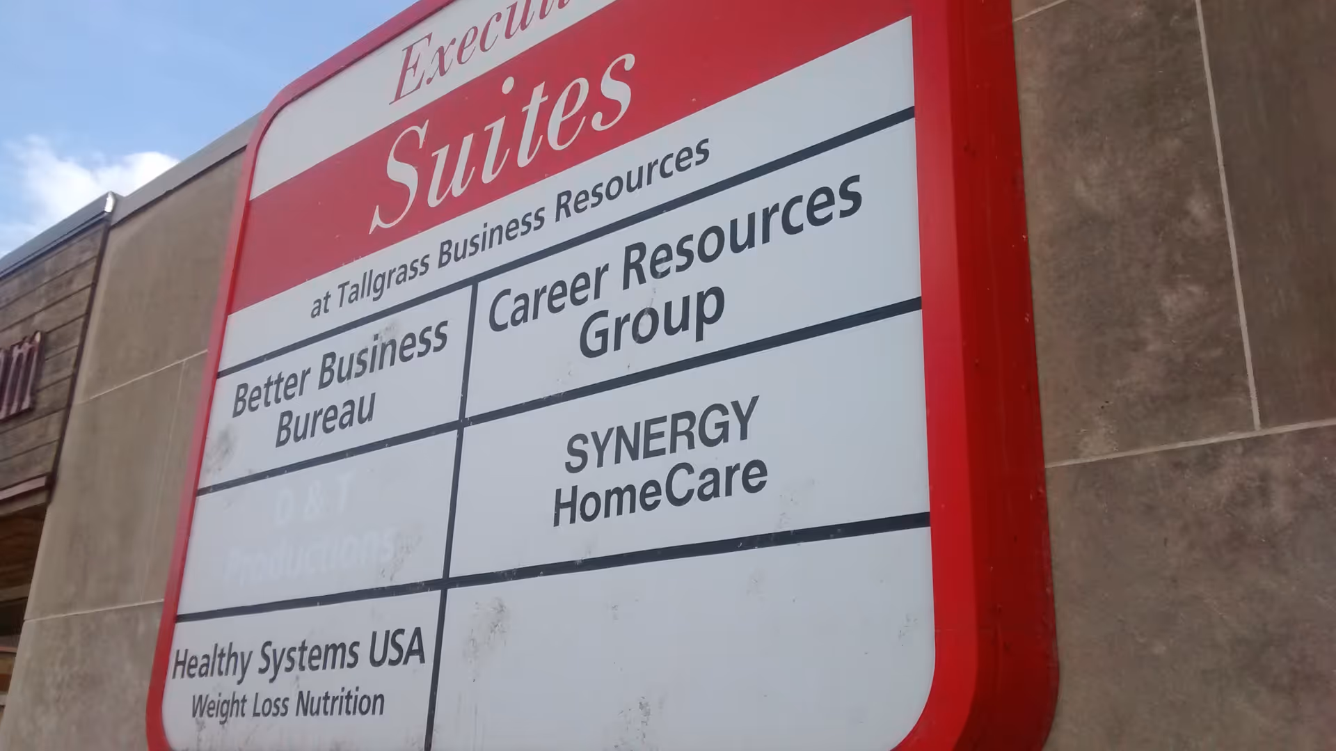 Red-framed signboard on a building exterior advertising SYNERGY HomeCare and other businesses.
