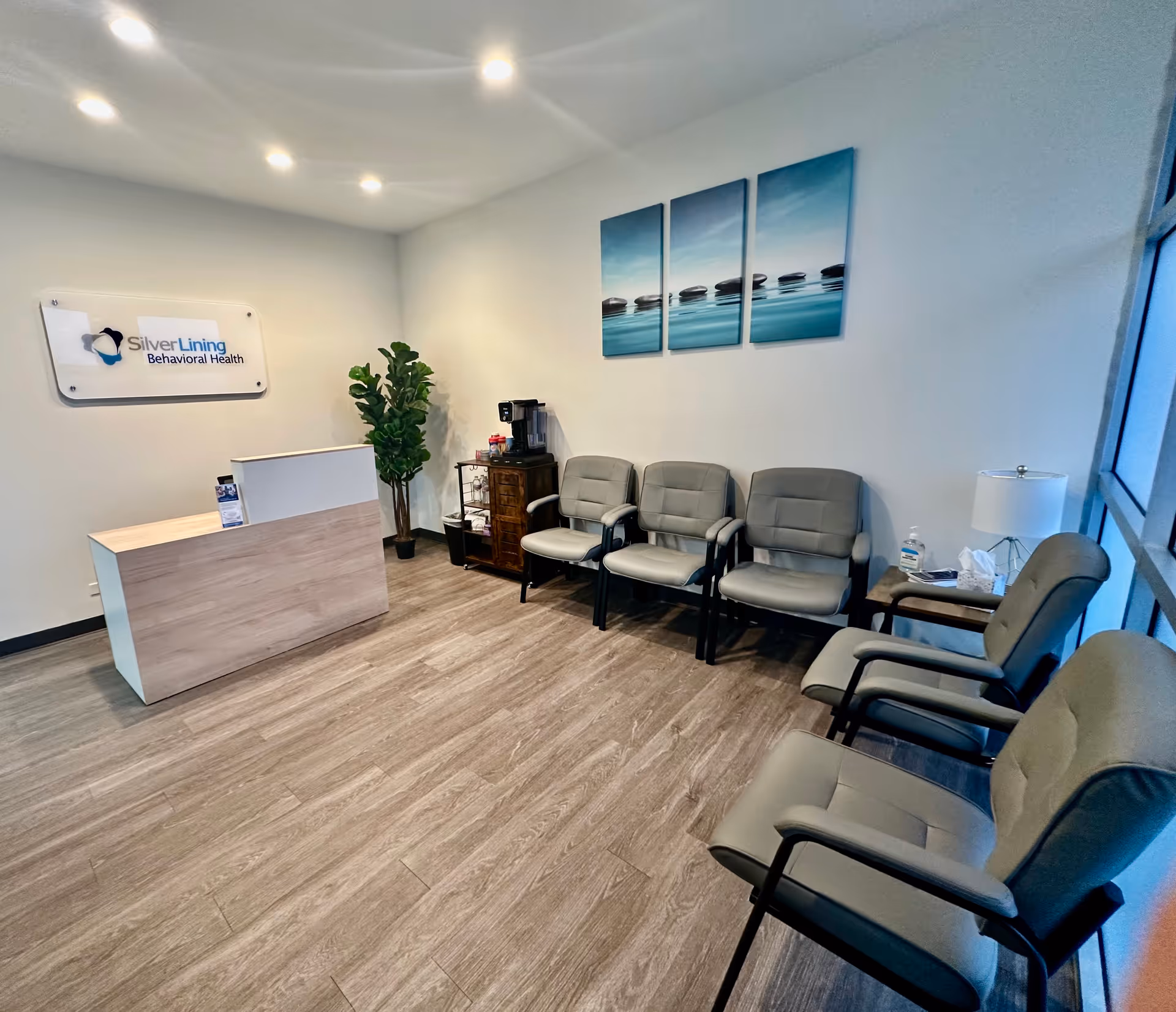 Reception desk in a bright waiting area with gray chairs and wall art.