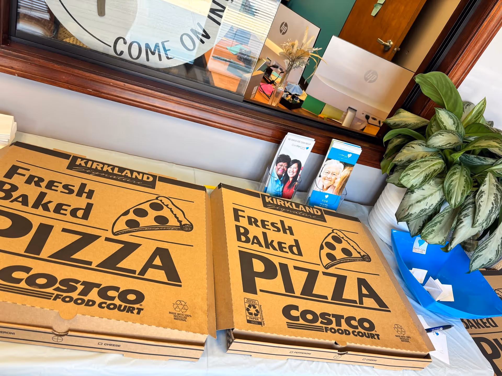 Indoor facility counter area with large pizza boxes, brochures, a plant, and a windowed service desk.