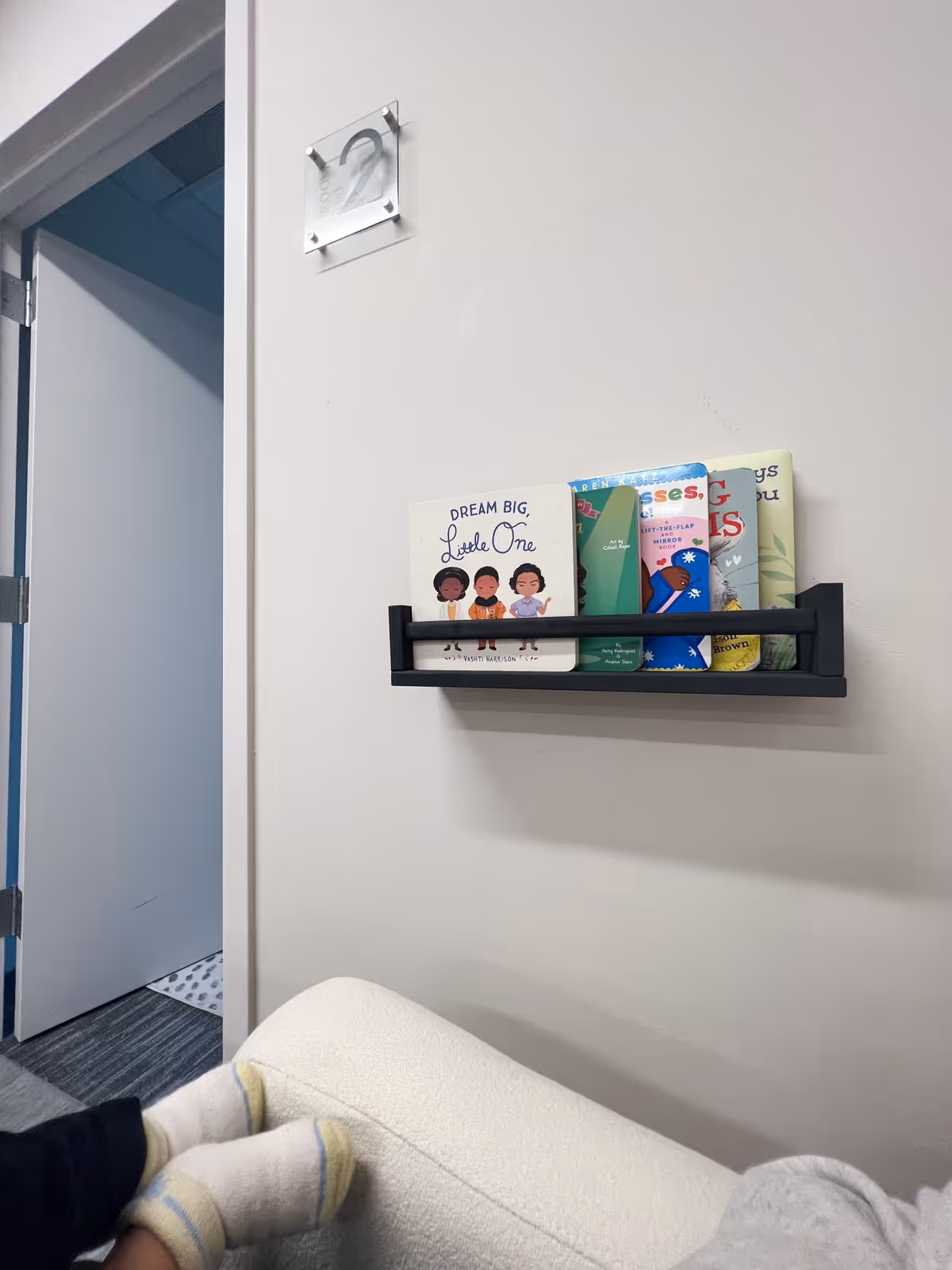 A wall shelf with children's books sits above a couch in a cozy living room.