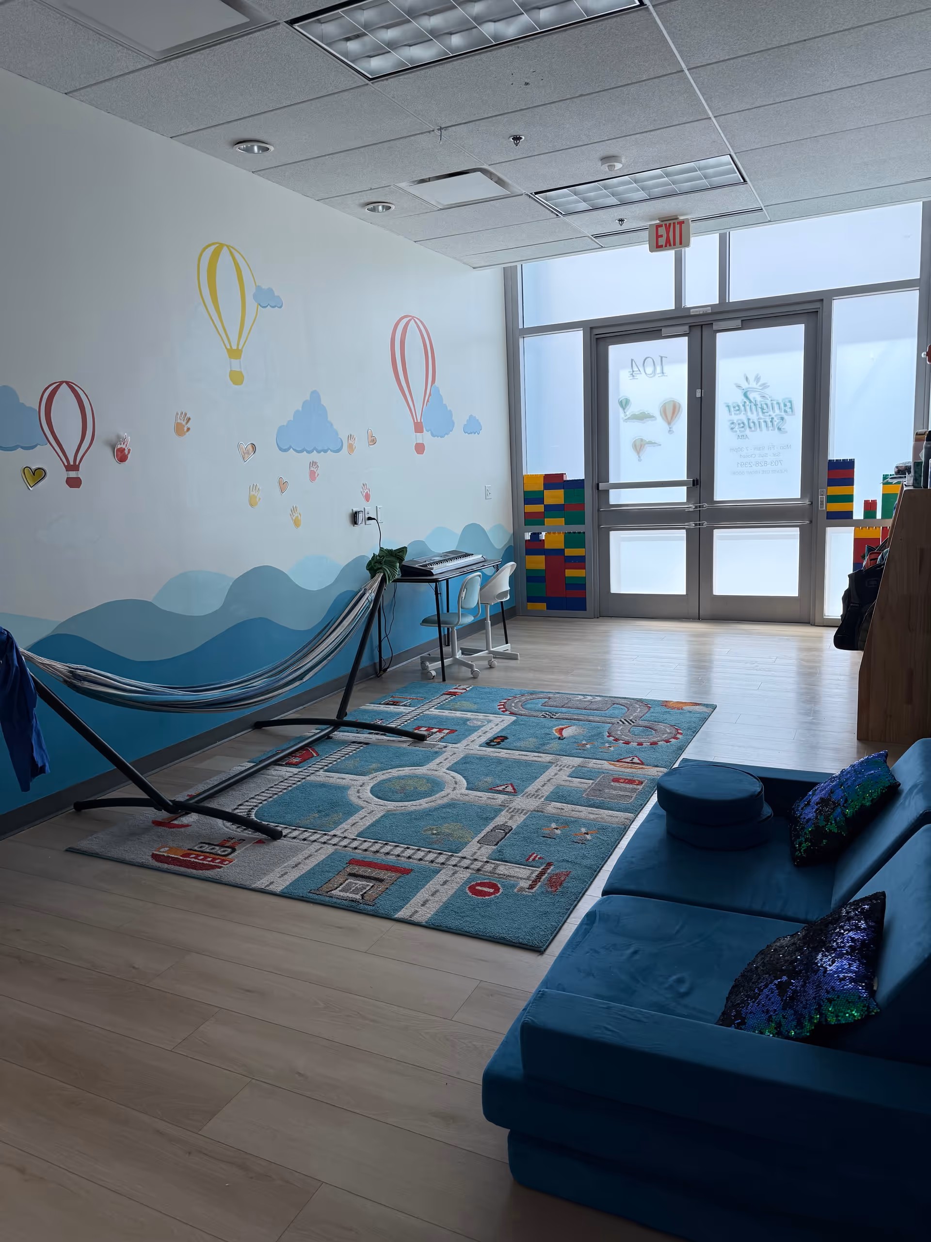 Bright playroom with mural walls, rug, blue couch, and therapy equipment near entrance