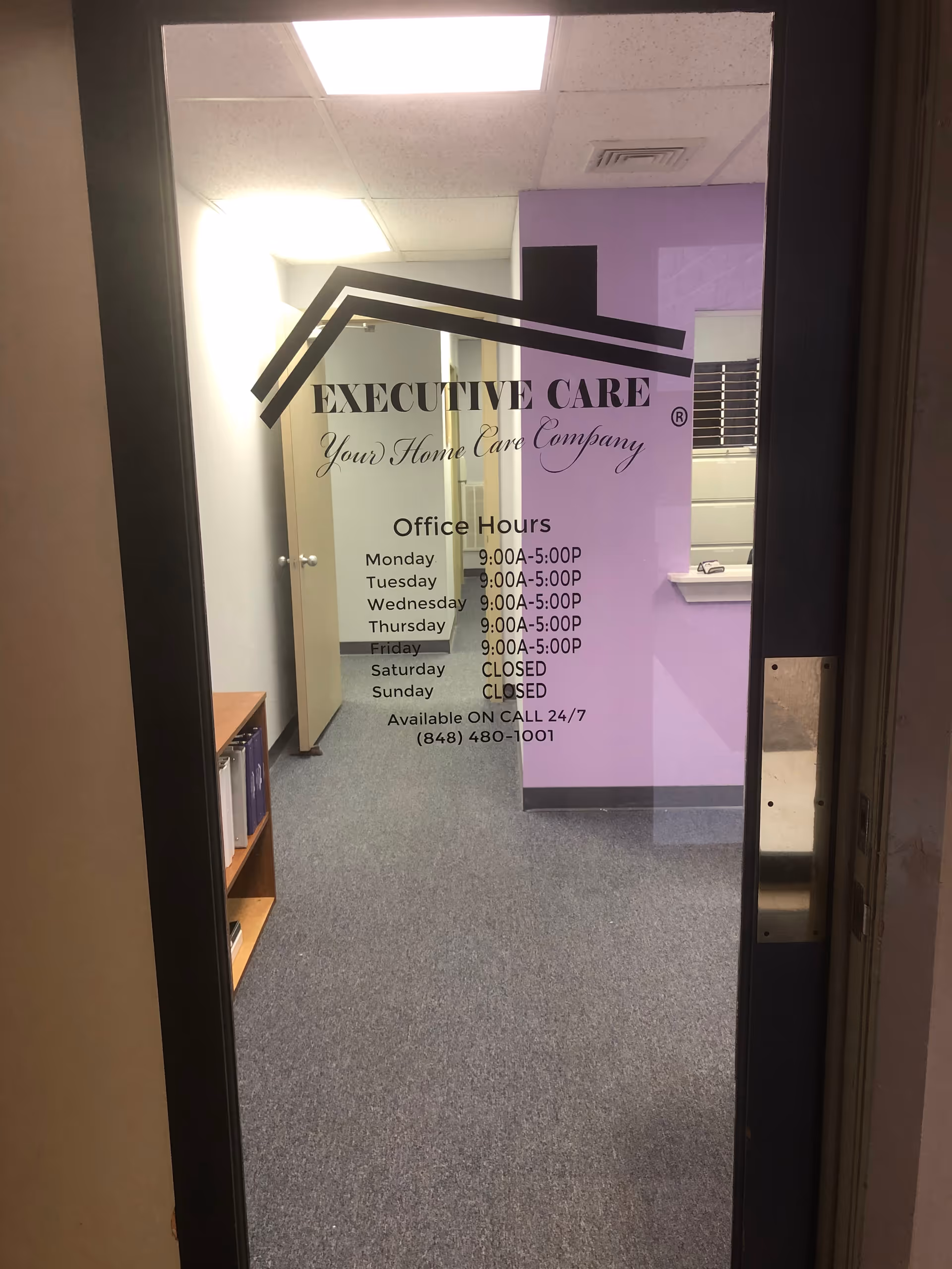 Glass door with Executive Care office hours sign and purple walls inside a facility.