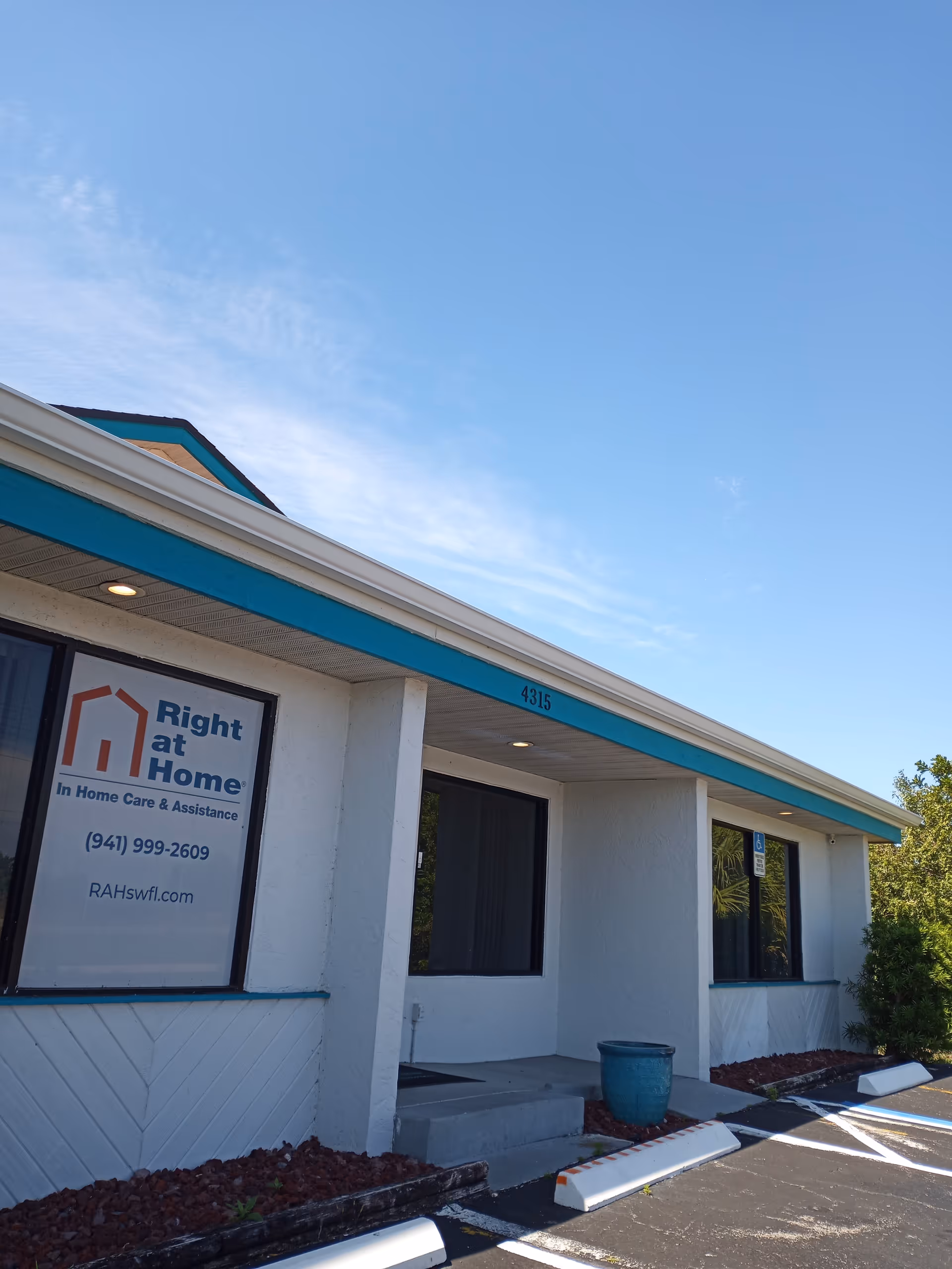 Front exterior of a Right at Home facility with sign, parking, blue sky.