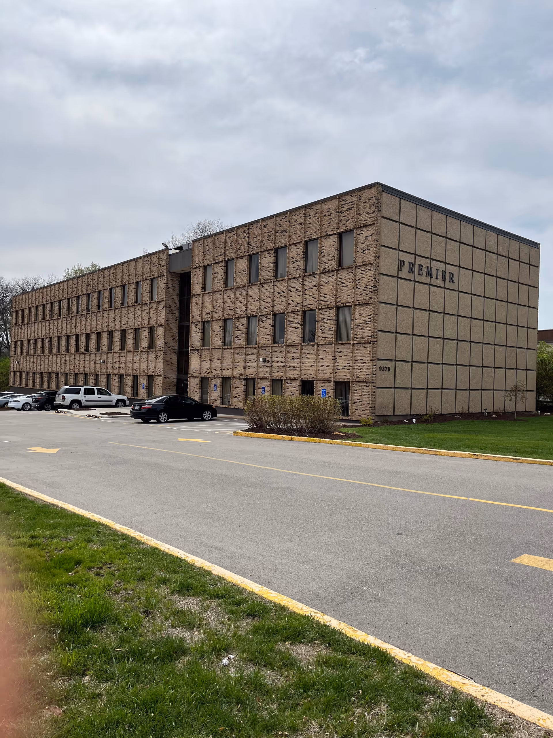 Exterior brick senior living building with a parking lot and grassy area.