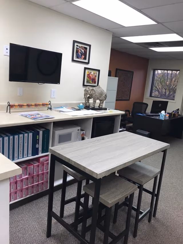 Interior reception area featuring a wall-mounted TV, decorative elephant statue, and a high worktable with stools.