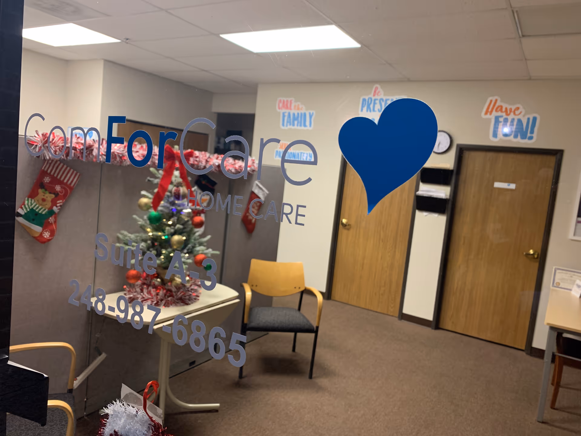 Interior office area with glass door, blue heart, festive tree, and seating.