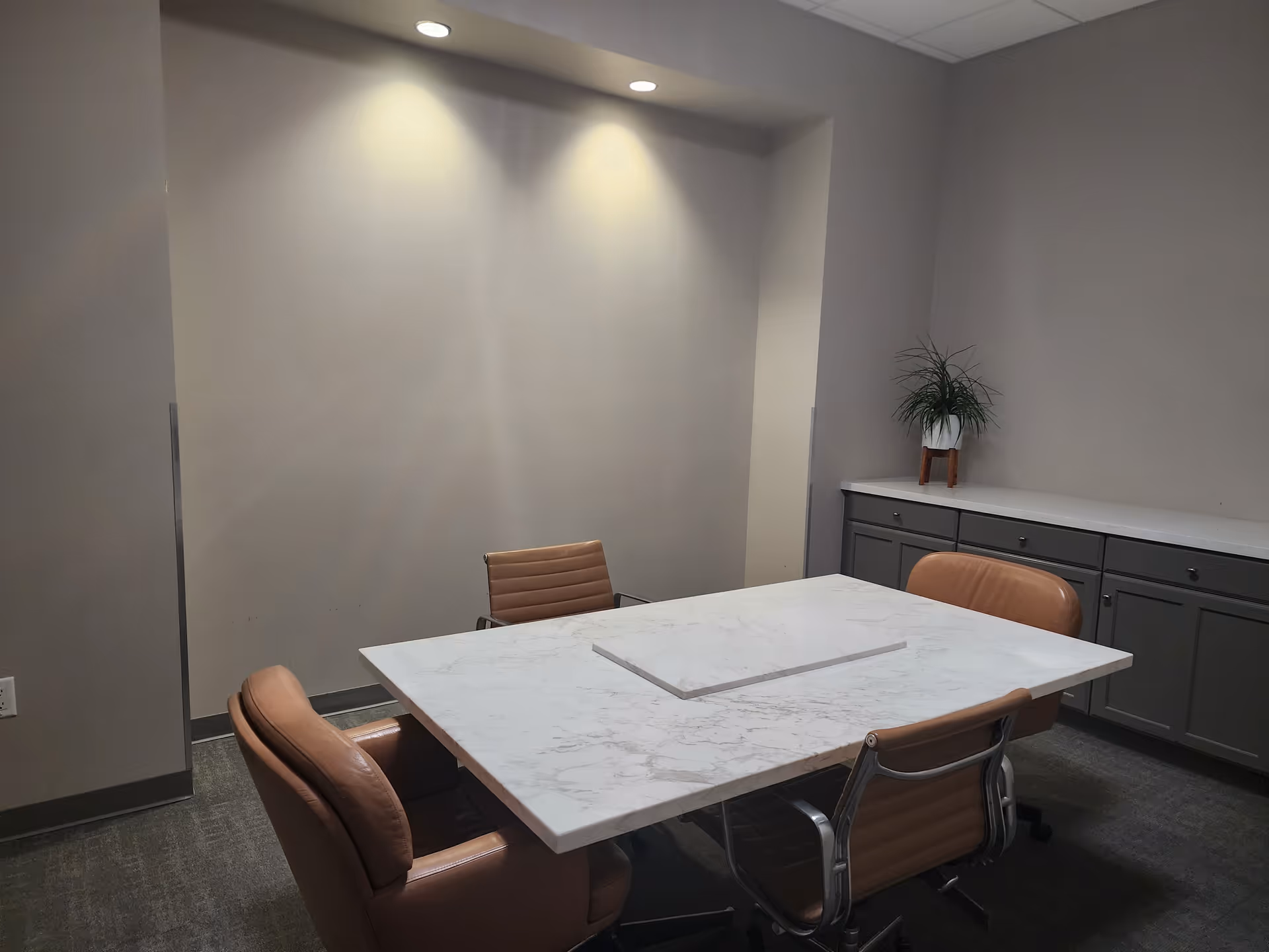A small conference room with a marble table, four brown leather chairs, and gray cabinets.