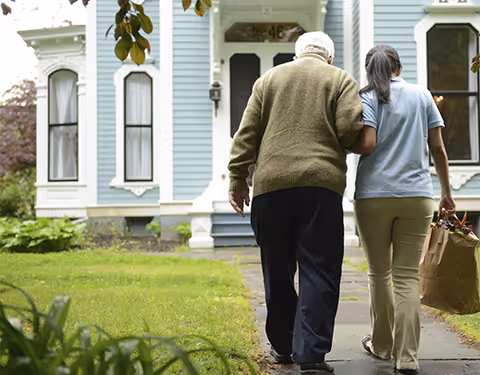 Two people walk toward the front entrance of a blue, ornate senior facility.