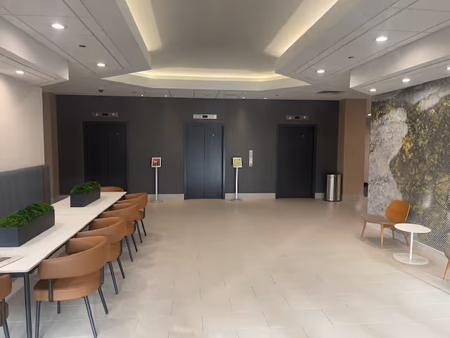 Modern lobby with desks, seating, and three elevator doors at the back.