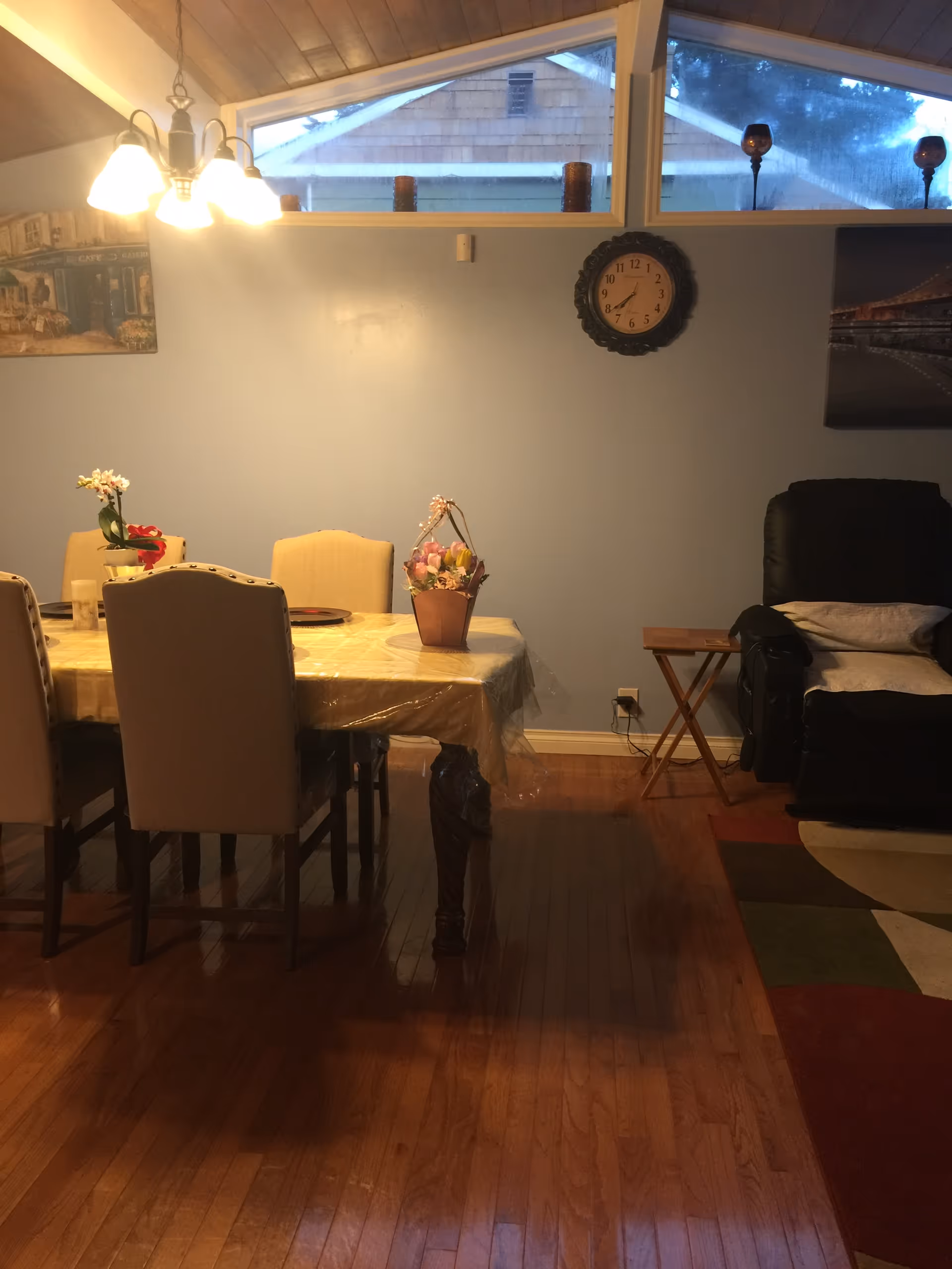 Cozy dining room with a table and chairs, flowers, wall clock, and a recliner.