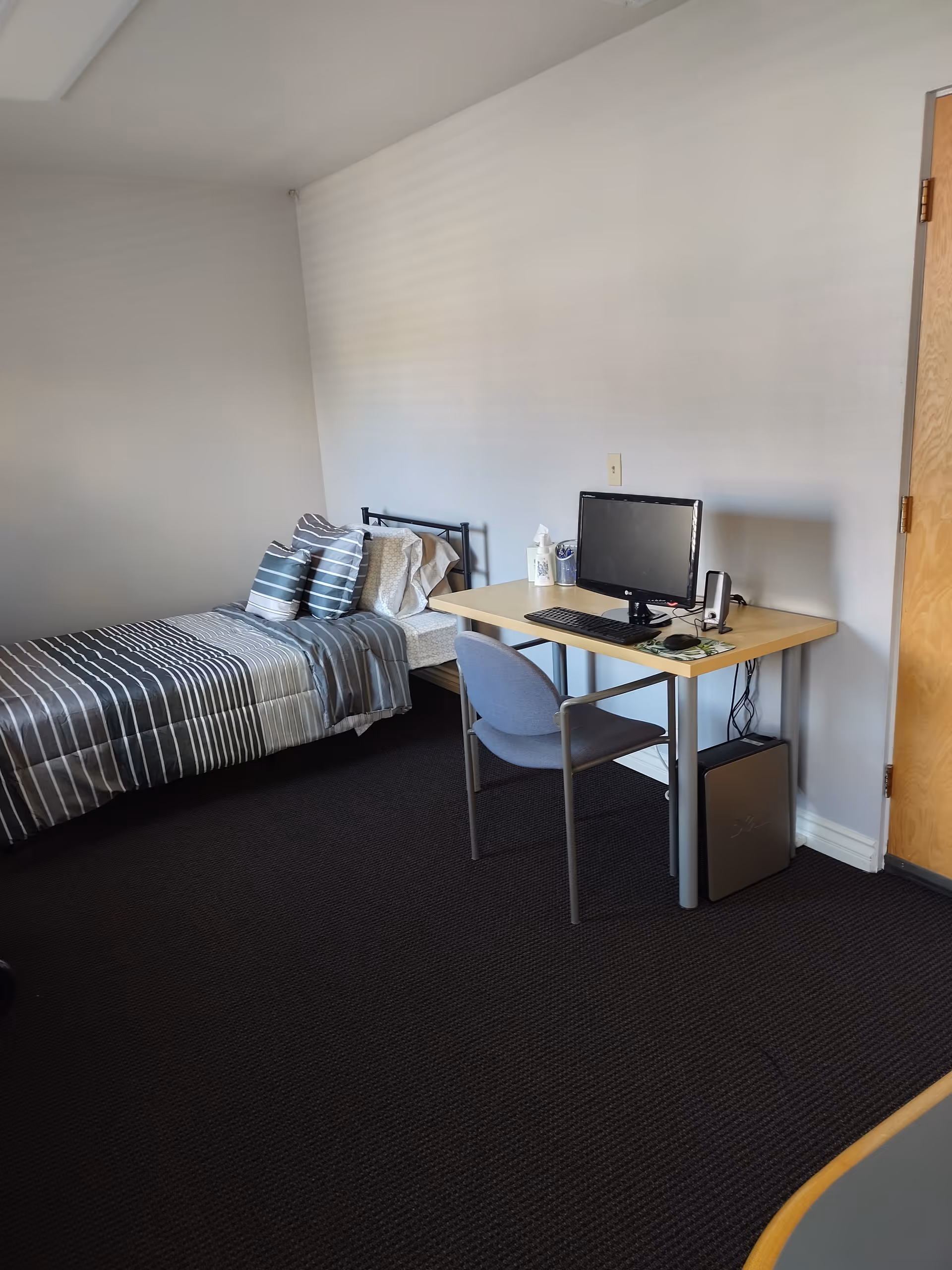 Compact bedroom with bed, desk, computer, and chair in a senior home.