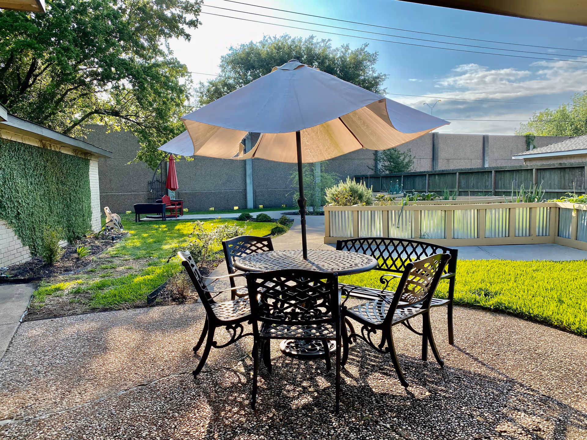 Outdoor patio with a metal table, chairs, and large umbrella in a sunny courtyard.