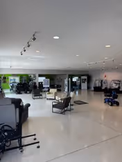 Open interior showroom displaying seating, mobility scooters, wheelchairs, and a bright reception area.
