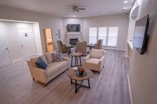 A bright, modern living room in a senior facility with sofas, chairs, and a TV.