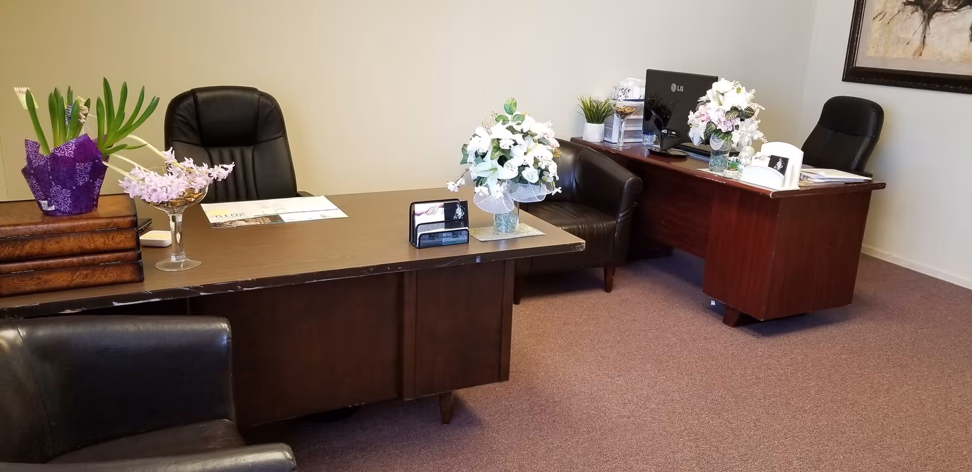 A furnished reception area with desks, chairs, and floral arrangements inside.