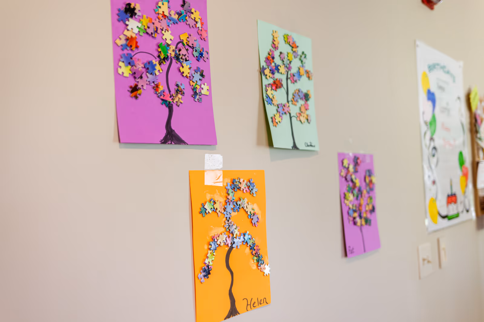 Colorful paper tree crafts displayed on a beige hallway wall inside a facility.