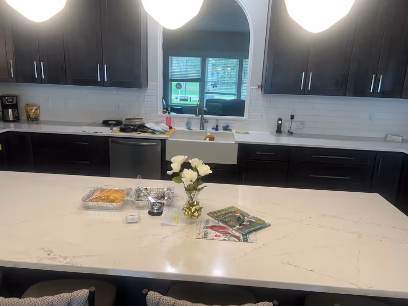 Modern kitchen with dark cabinets, white countertops, island centerpiece, sink, and magazines on the island.