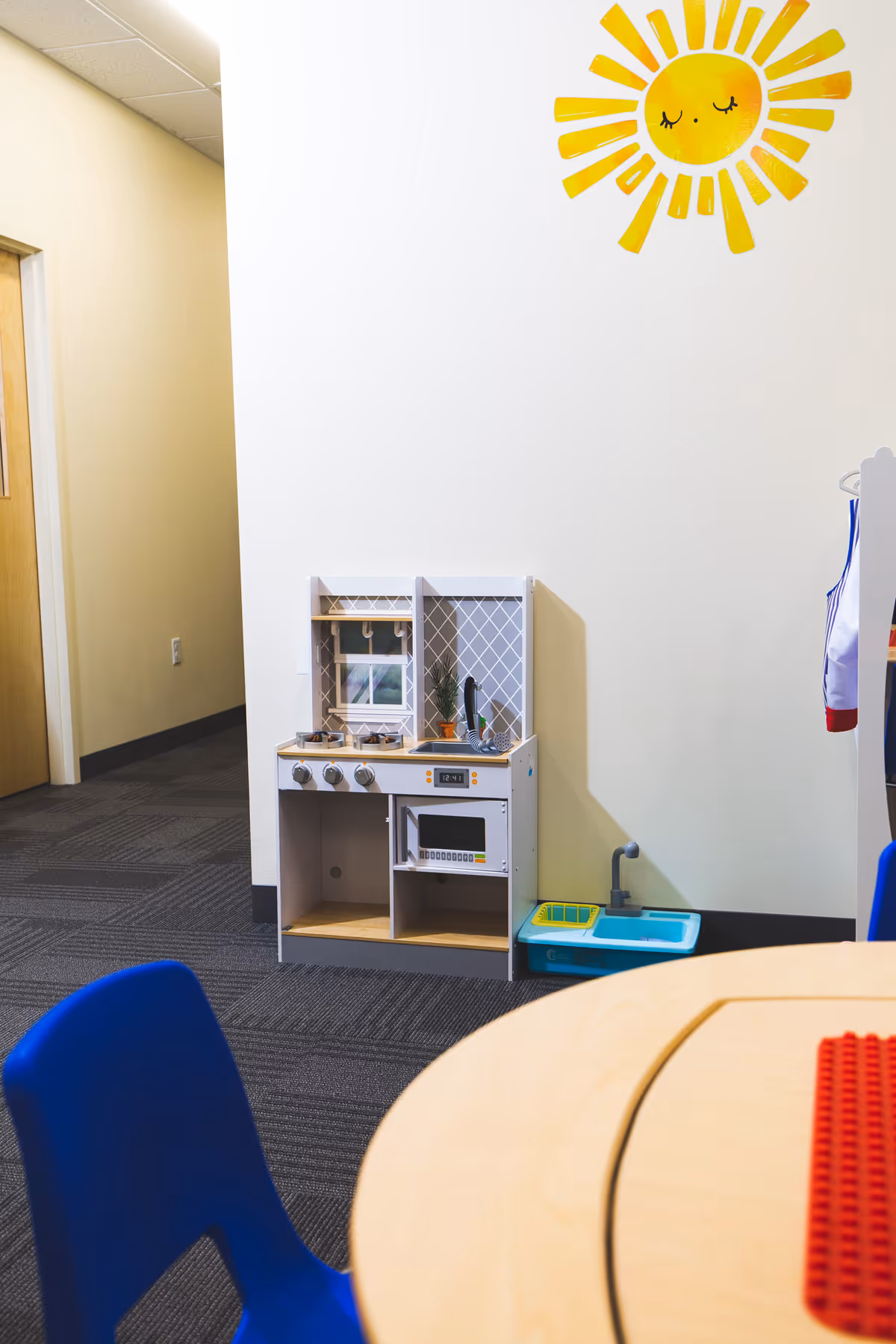 A small play kitchen sits in a bright room beneath a sun wall art.
