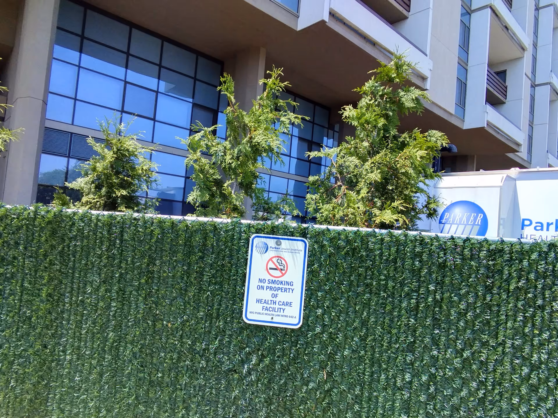 Exterior view of Parker Jewish Institute building with hedges, trees, and a no-smoking sign.