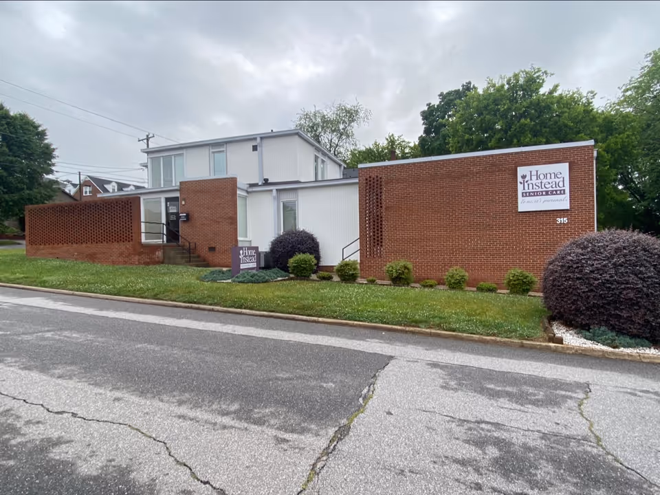 Brick exterior of Home Instead Senior Care building with a sign and trimmed shrubs.