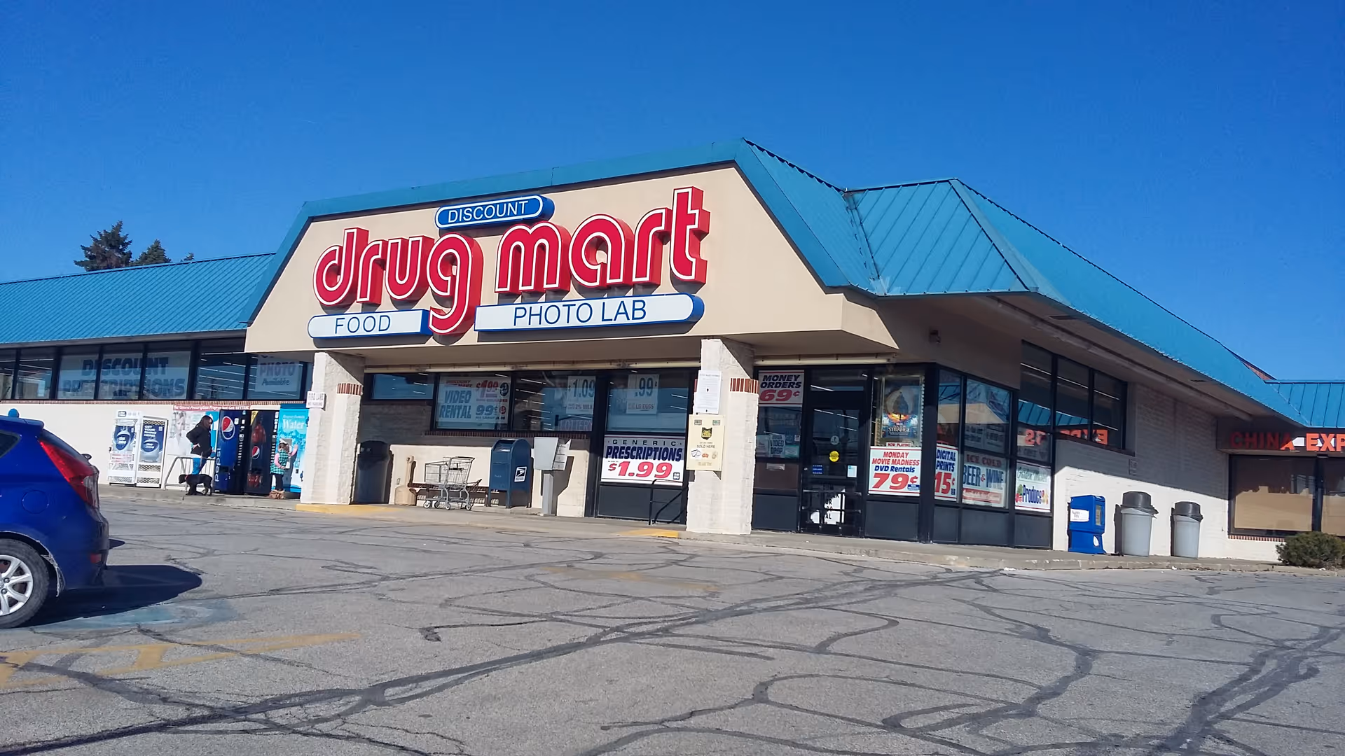 Front view of Discount Drug Mart storefront with blue awning and parking lot.