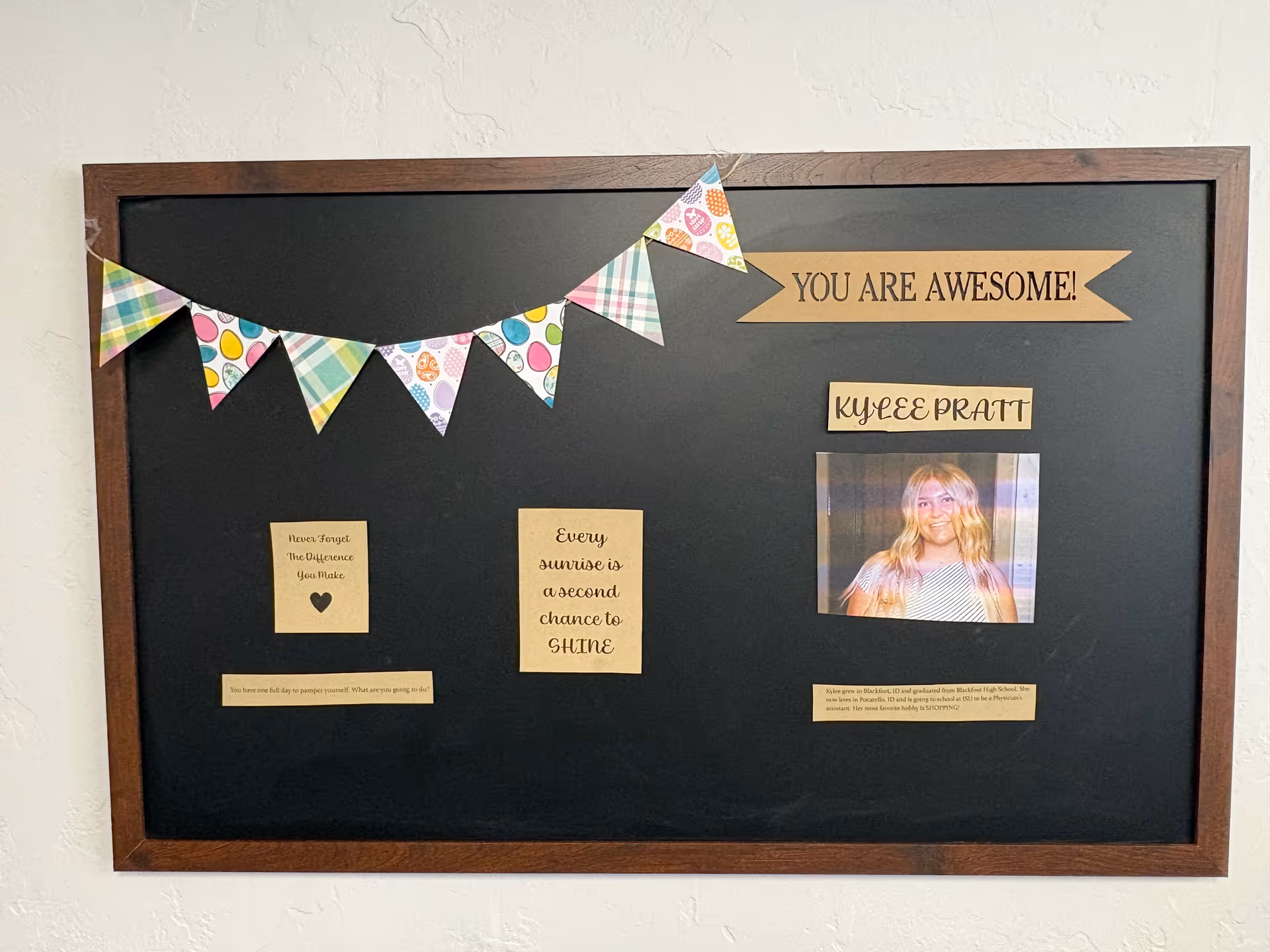 Framed black bulletin board with bunting, quotes, and a photo on the wall.