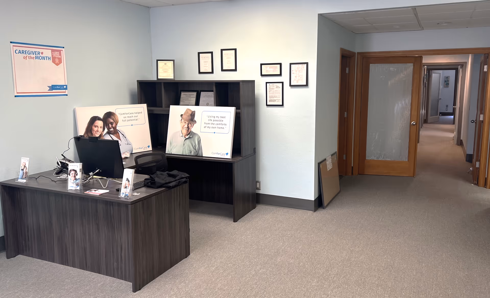 Reception area with a desk, computer, and 'Caregiver of the Month' posters.